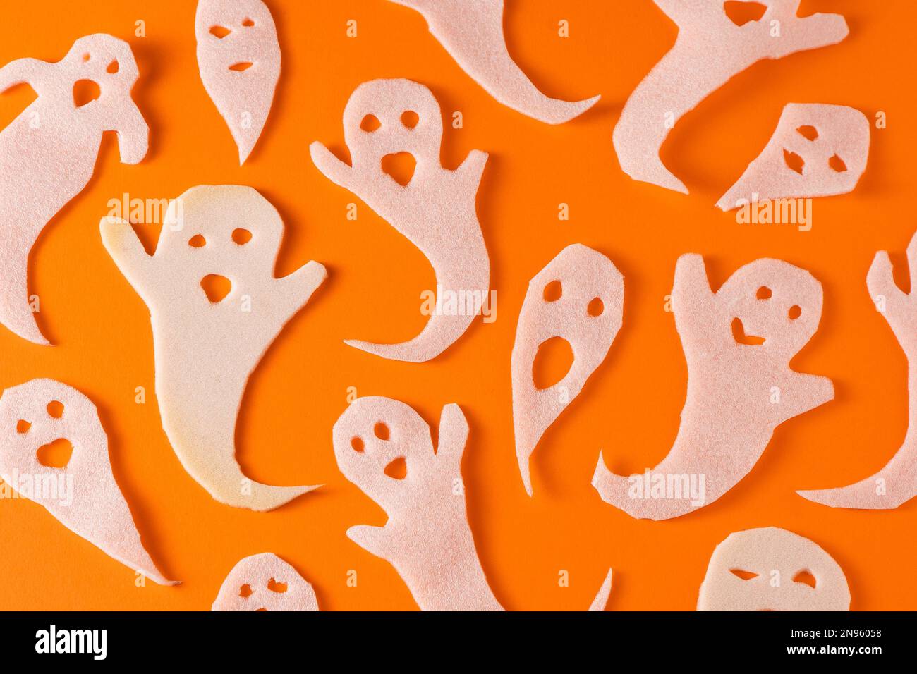 Fantasmi bianchi bambini di mestiere per Halloween. Immagine fantasma della carta di avvolgimento su sfondo arancione vista dall'alto. Un mostro pauroso e divertente giocattolo con le tue mani. Fumetto Creepy Whisper. Fai-da-te fatto a mano. Impostare i caratteri boo Foto Stock