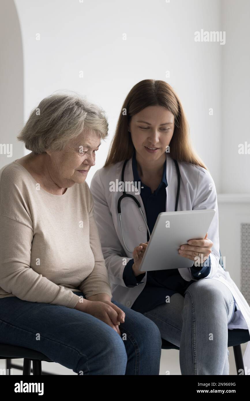 Medico positivo amichevole che mostra lo schermo della compressa a un paziente anziano 80s Foto Stock