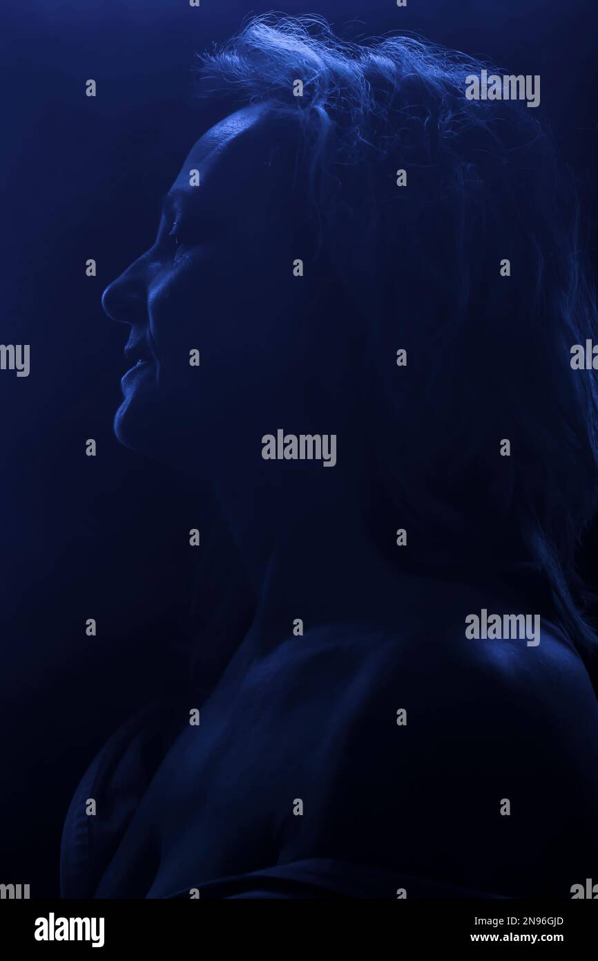 Ritratto retroilluminato di una donna bionda di mezza età in luce blu Foto Stock