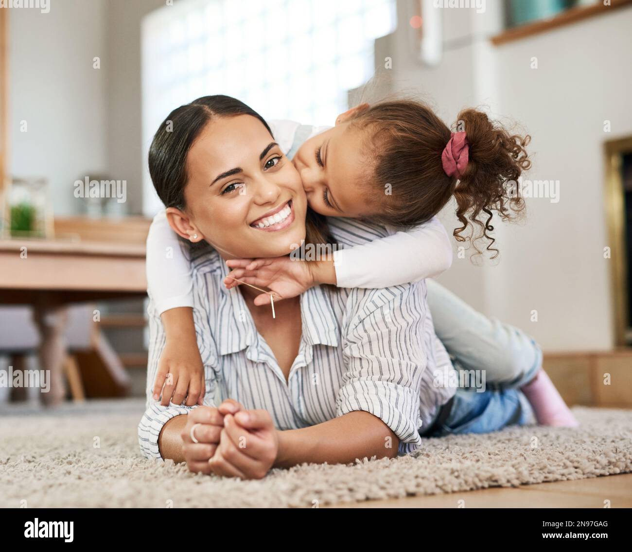 Beati ad essere tanto amati. una bambina che dà alla madre un bacio sulla guancia mentre si rilassa insieme a casa. Foto Stock