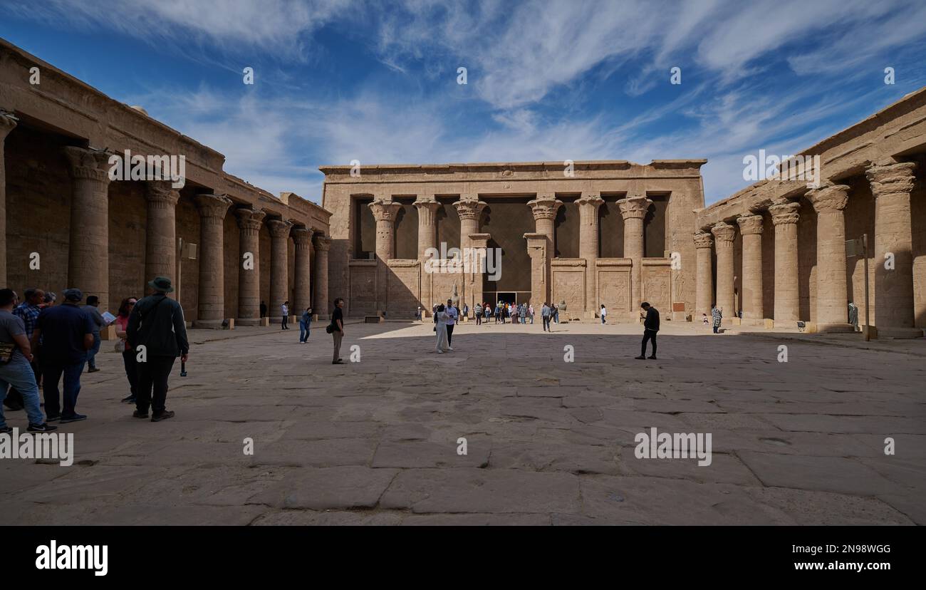 Tempio di Edfu lato nord corte, Edfu, Egitto vista luce del giorno con turisti e nuvole nel cielo Foto Stock
