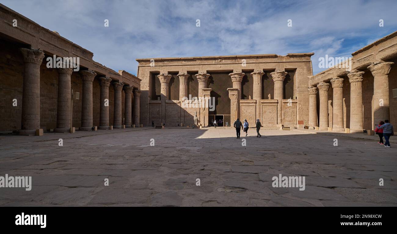 Tempio di Edfu lato nord corte, Edfu, Egitto vista luce del giorno con turisti e nuvole nel cielo Foto Stock