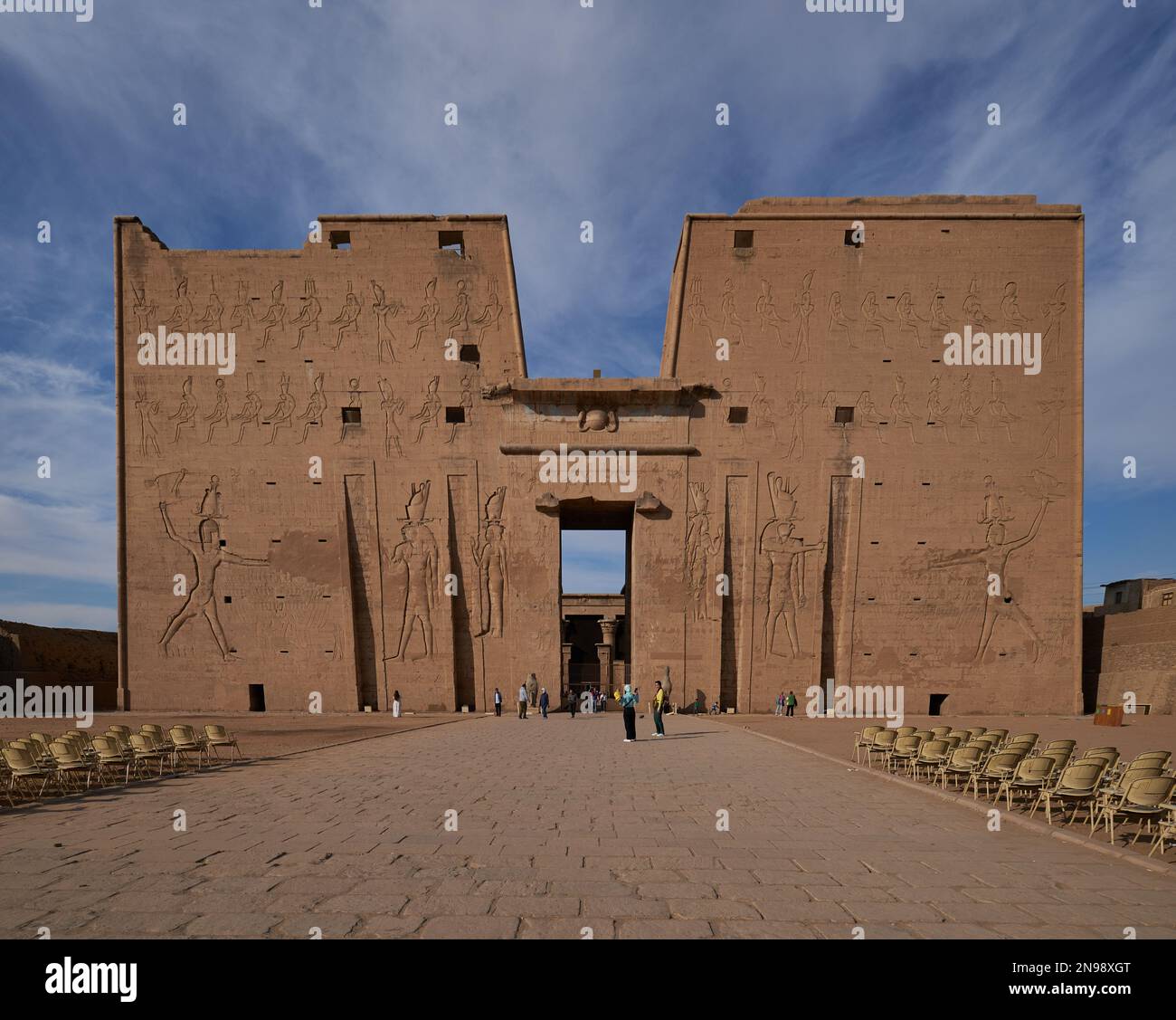 Il Tempio di Edfu a Edfu, Egitto, vista esterna della luce del giorno che mostra l'ingresso principale con i visitatori e le nuvole nel cielo sullo sfondo Foto Stock