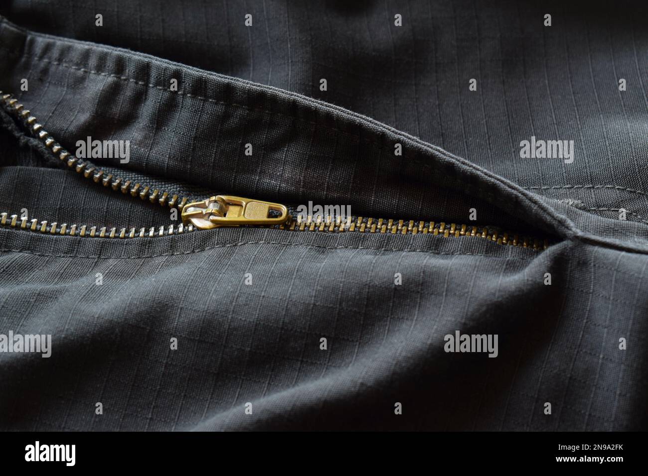Primo piano di una zip semi aperta in oro su pantaloni neri. Foto Stock