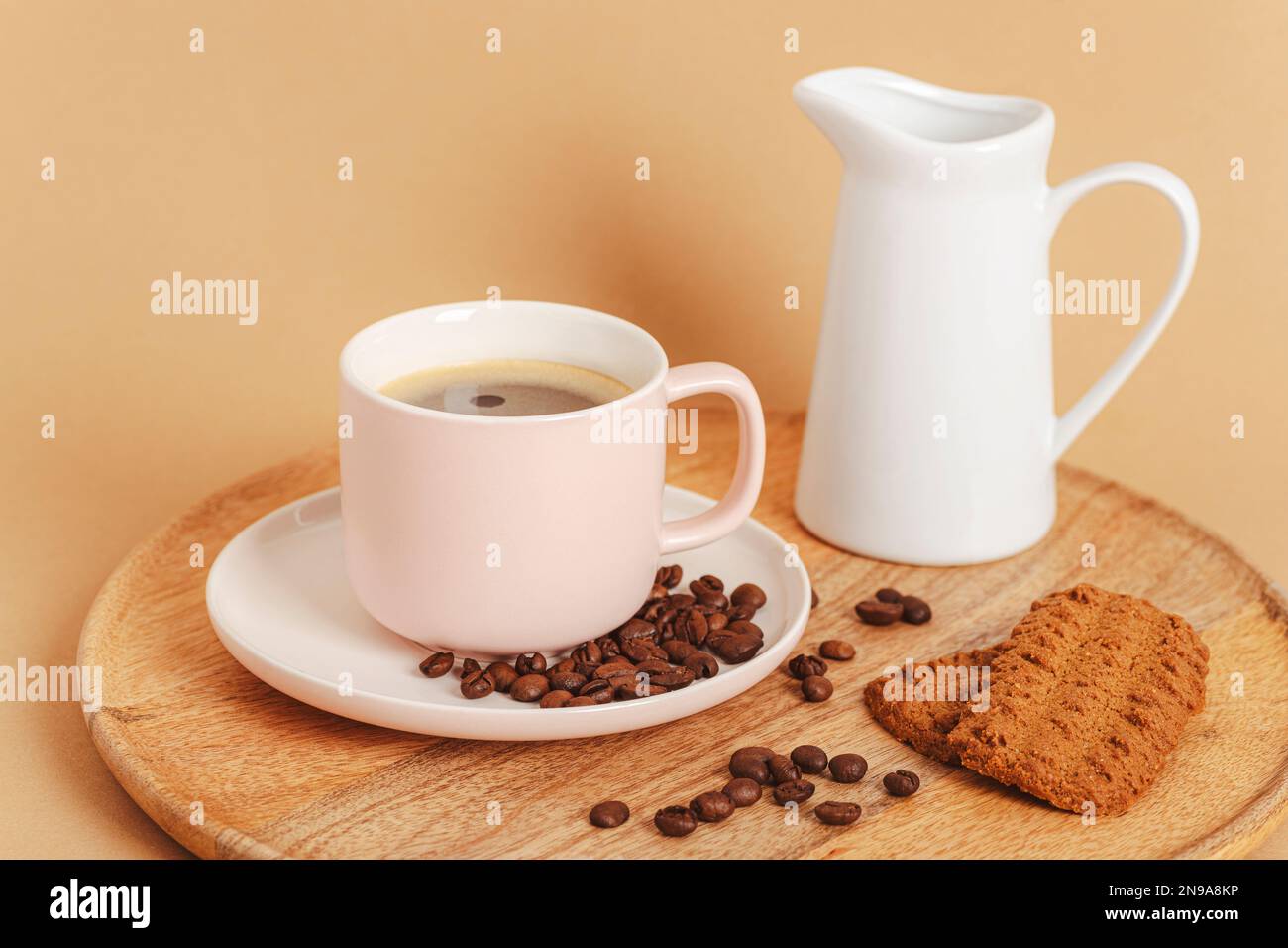 Tazza di caffè, chicchi di caffè tostati, biscotti e caraffa con latte su un vassoio di legno Concetto di colazione mattutina. Primo piano. Foto Stock
