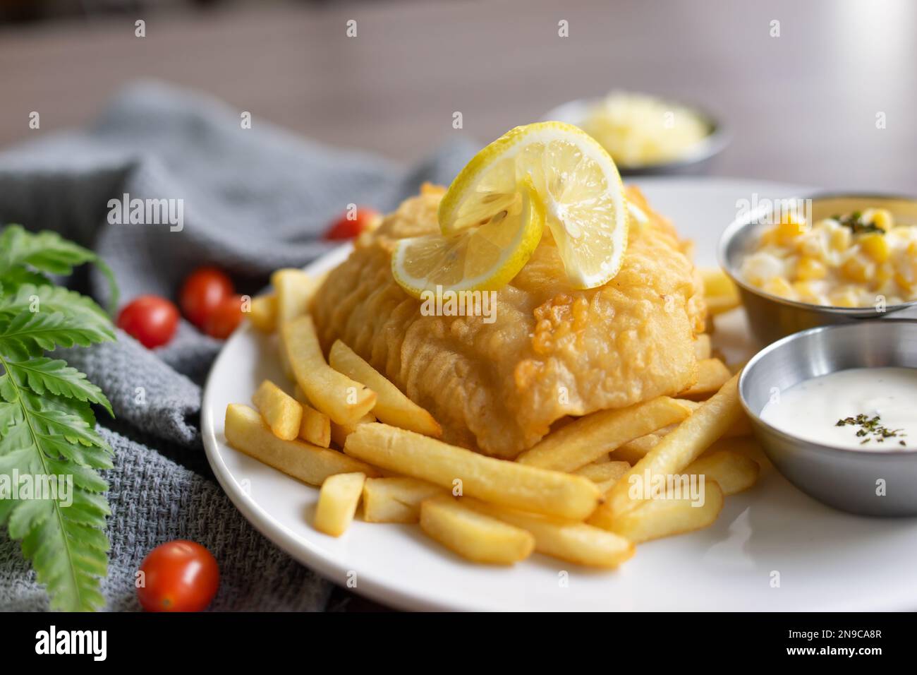 Un pezzo di pesce in pastella con patatine fritte su un piatto bianco su un tavolo di legno Foto Stock