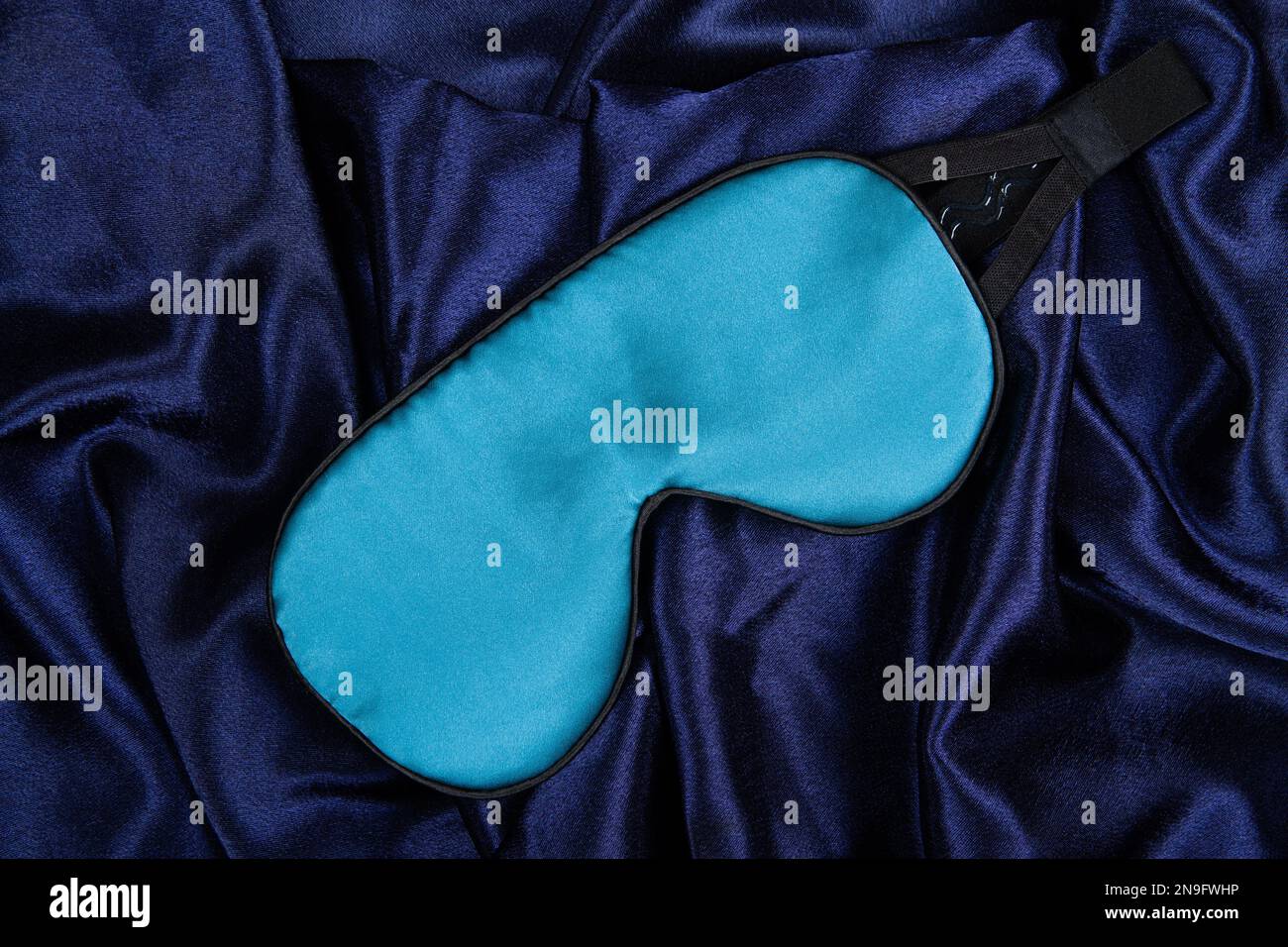 La maschera di seta blu chiaro si trova su sfondo blu scuro e serico Foto Stock