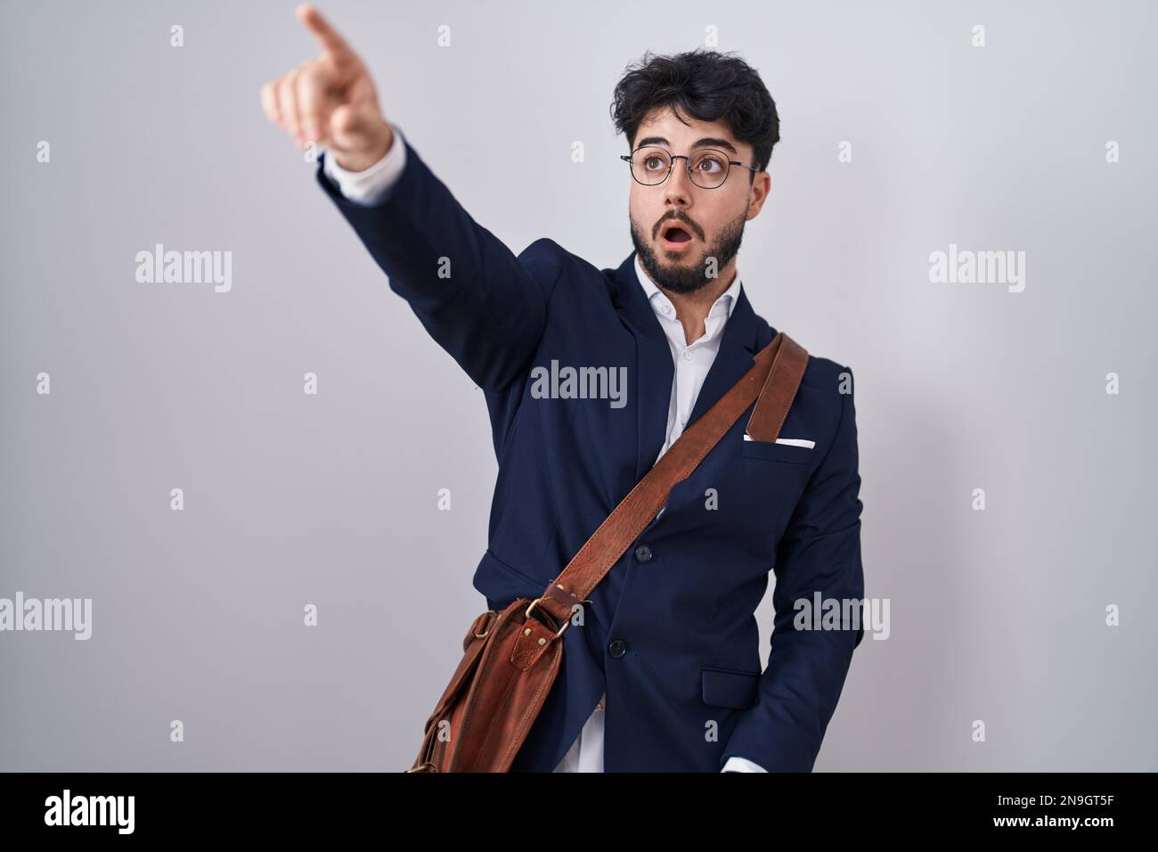 Uomo ispanico con barba che indossa abiti da lavoro puntando con il dito sorpreso davanti, bocca aperta stupita espressione, qualcosa sul fronte Foto Stock