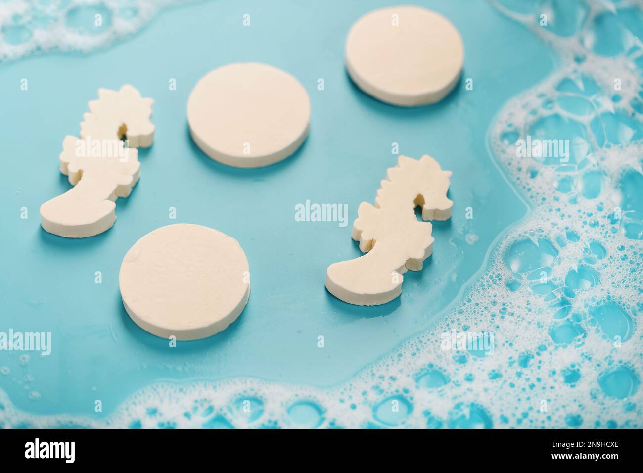 Sapone a forma di cavalluccio marino e cerchi con schiuma su sfondo blu Foto Stock