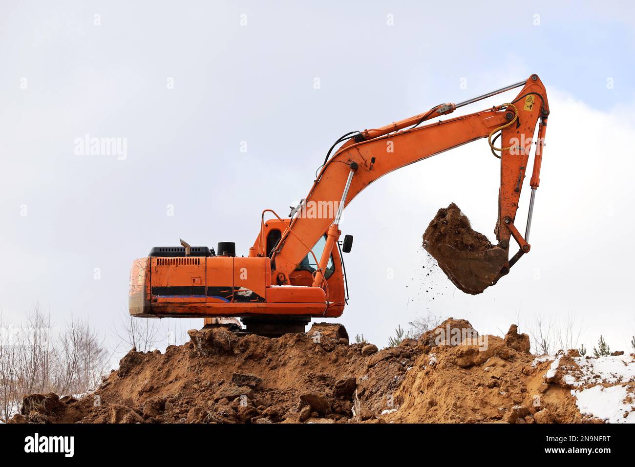 L'escavatore cingolato scarta il terreno con una benna. Lavori di movimento terra, industria di scavo e di costruzione Foto Stock