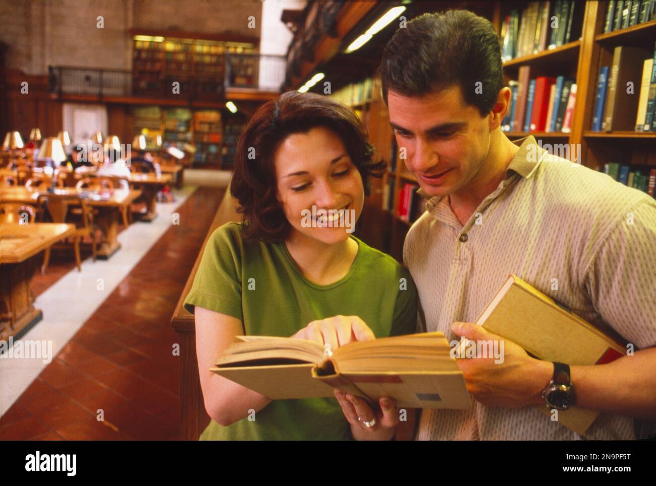 Coppia più giovane in una biblioteca, guardando un libro mentre la donna punta a qualcosa Foto Stock