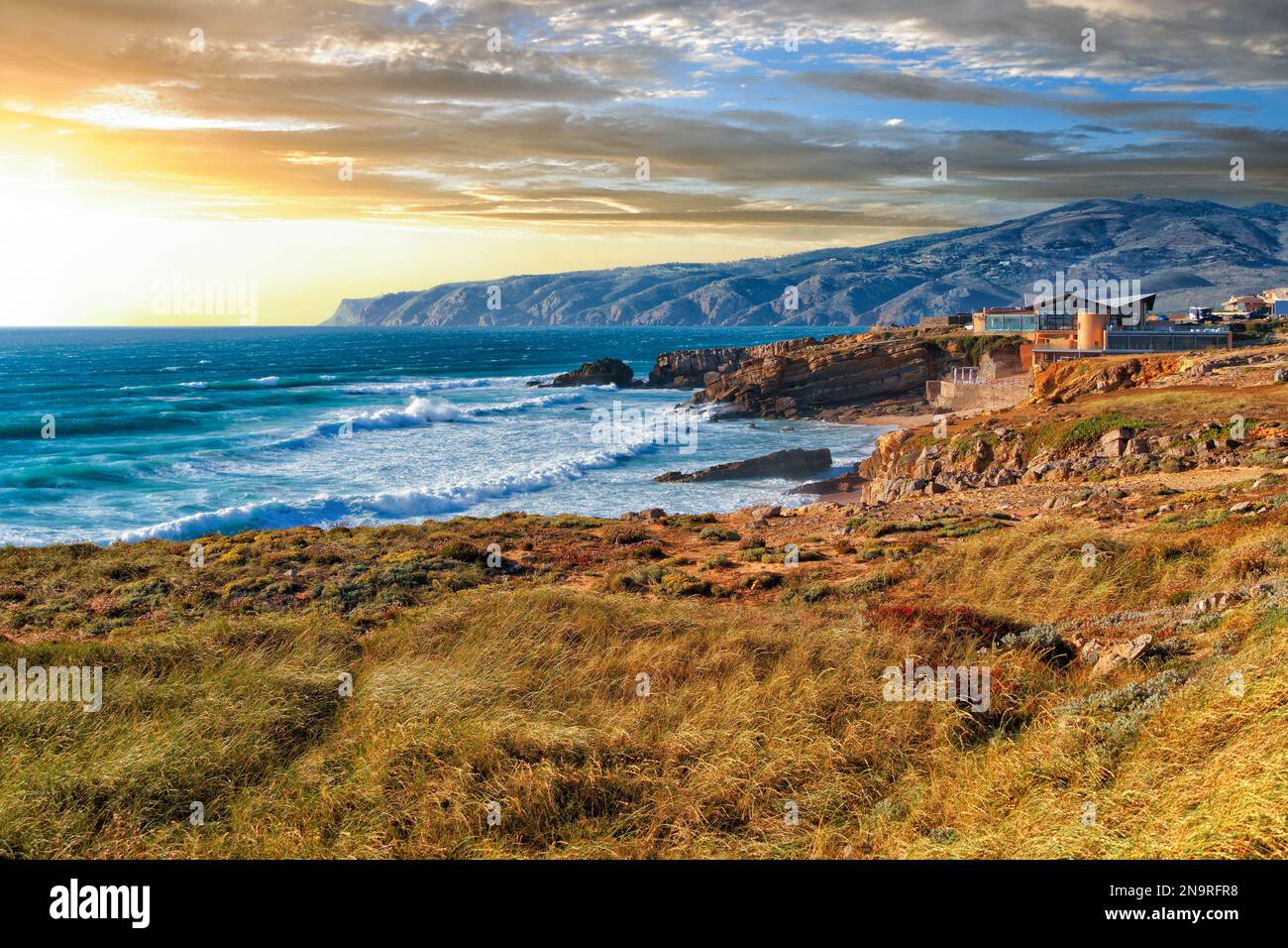 Pittoresco paesaggio del tramonto sulla costa rocciosa dell'infuocato Oceano Atlantico vicino a Capo Roca alla luce del sole che tramonta in Portogallo. Comune Foto Stock