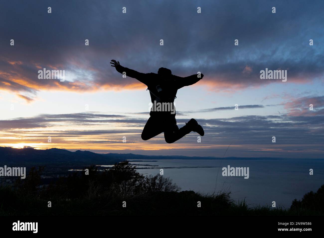 La silhouette di un uomo che ovviamente salta giù per una montagna con uno sfondo mozzafiato Foto Stock