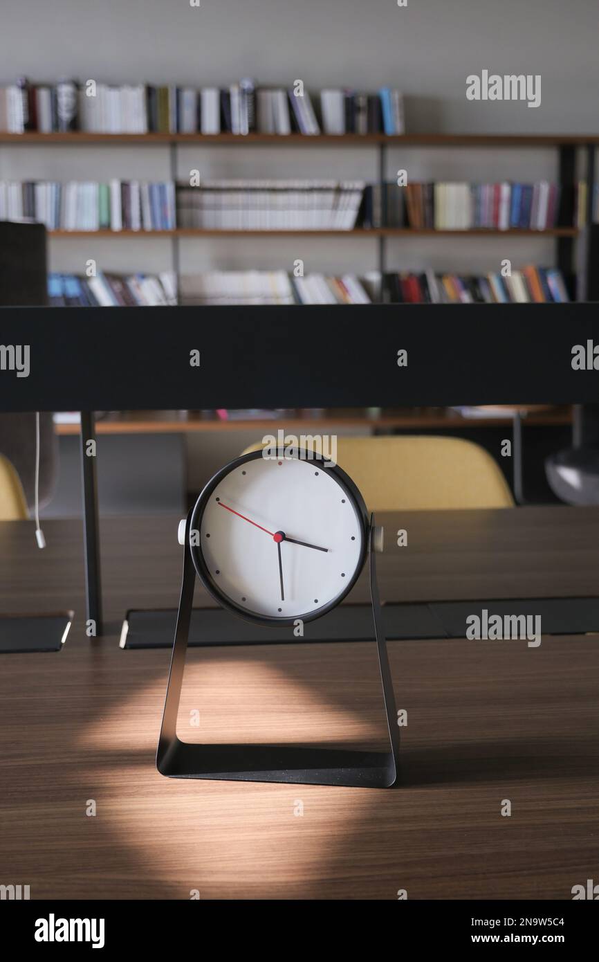 Orologio sul tavolo sullo sfondo di una biblioteca Foto Stock