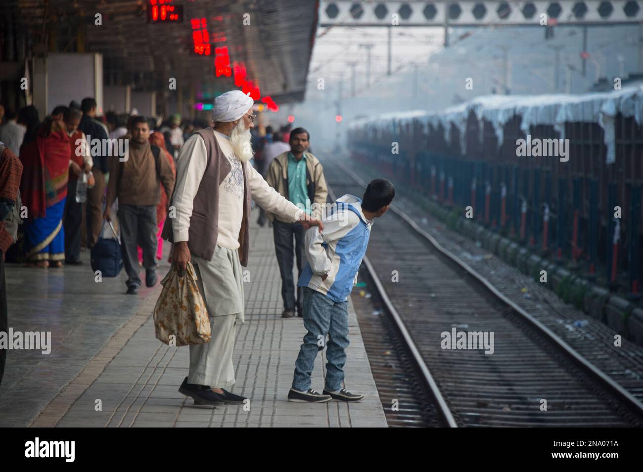 Un uomo anziano che tiene un bambino lontano dai binari del treno a Chandigarh, India; Chandigarh, nuova Delhi, India Foto Stock