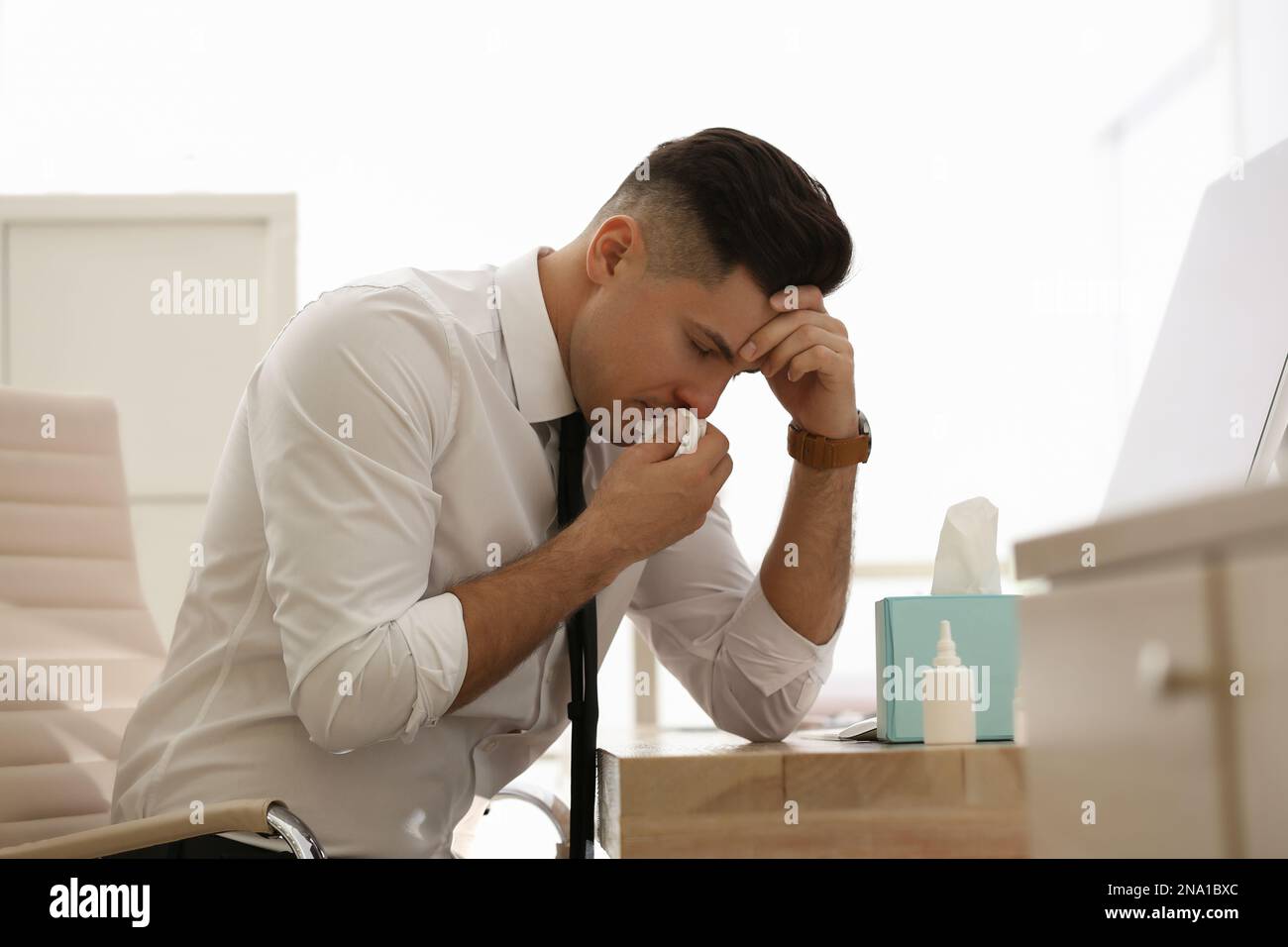 Uomo d'affari malato a tavola con spray nasale e scatola di carta fazzoletti in ufficio Foto Stock