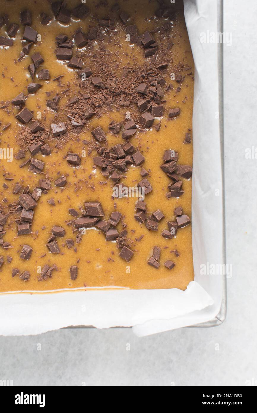 Pastella blondie con gocce di cioccolato in una teglia da forno quadrata rivestita con pergamena, pastella per torte in una teglia da forno da 10 cm Foto Stock