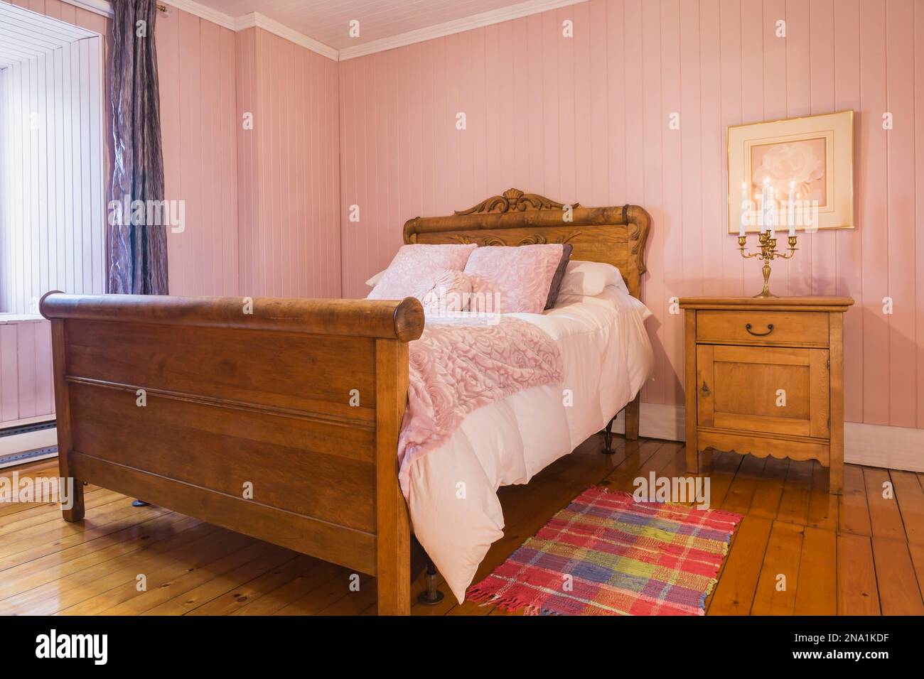 Letto a tre quarti con copriletto bianco e testiera e poggiapiedi in legno antico con dettagli intagliati, tavolino nella camera da letto con pareti in rosa. Foto Stock