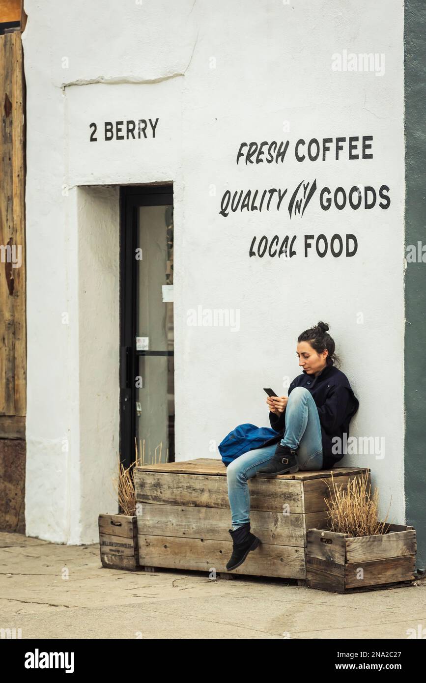 Giovane donna che usa il suo smartphone al di fuori di una caffetteria a Williamsburg; Brooklyn, New York, Stati Uniti d'America Foto Stock