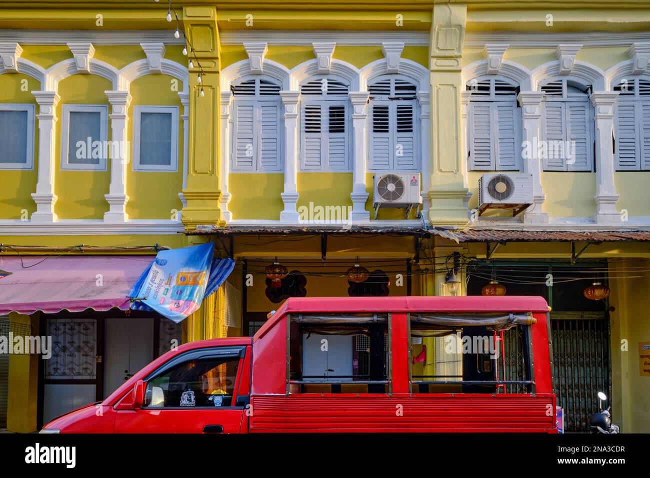 Colorate botteghe in stile sino-portoghese, con finestre ad arco e a graticcio, nella zona della Città Vecchia di Phuket, Thailandia; un tuk-tuk o un songthaew nel f/g. Foto Stock