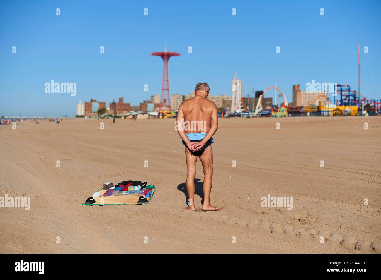 Uomo in costume da bagno che si estende sulla spiaggia di Coney Island; New York City, New York, Stati Uniti d'America Foto Stock