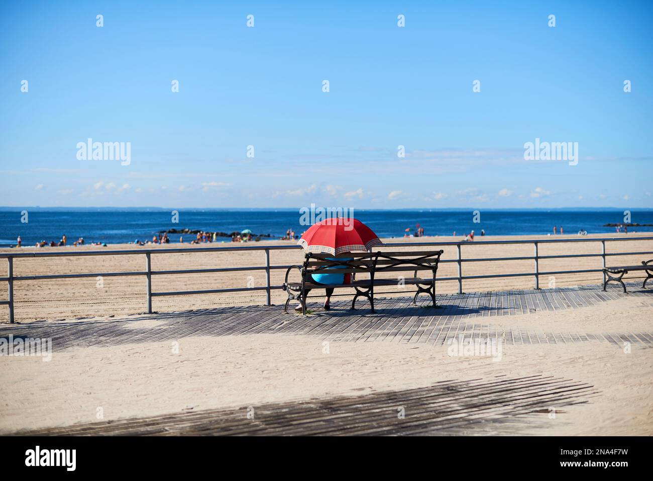 Donna seduta con ombrello sul lungomare di Coney Island che guarda all'Oceano Atlantico; New York City, New York, Stati Uniti d'America Foto Stock