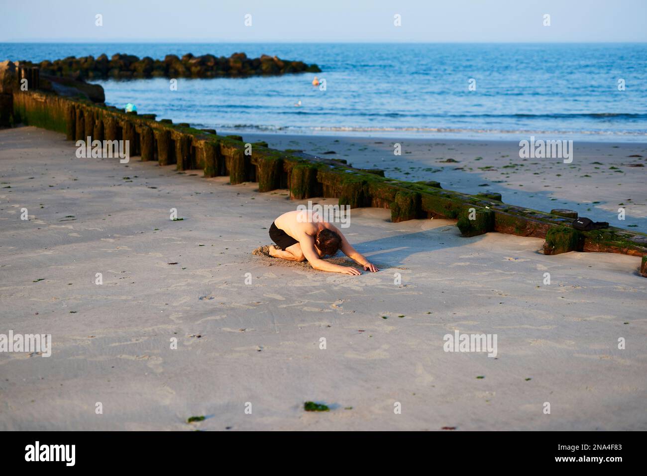 Uomo in costume da bagno che fa yoga la mattina presto su Coney Island Beach; New York City, New York, Stati Uniti d'America Foto Stock