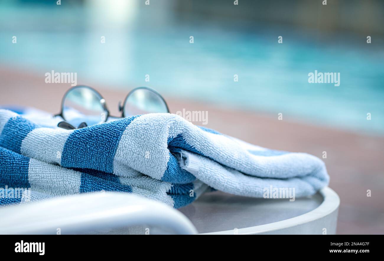Telo da piscina su poltrona con occhiali e sfondo piscina. Concetto di vacanza estiva. Foto Stock
