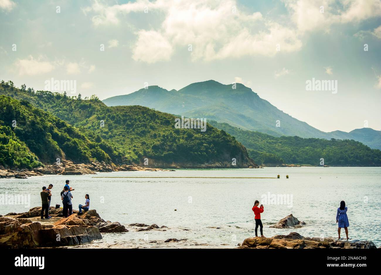 Persone che scattano foto su una spiaggia rurale su un'isola di Hong Kong con uno sfondo montuoso Foto Stock