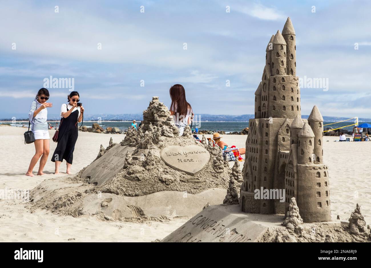 Due donne scattano una fotografia di un'altra donna in piedi accanto a una creazione di un castello di sabbia sulla spiaggia di Coronado Foto Stock
