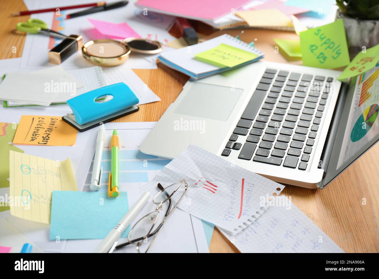 Tavolo caotico con computer portatile e cancelleria. Concetto di essere sopraffatto dal lavoro Foto Stock