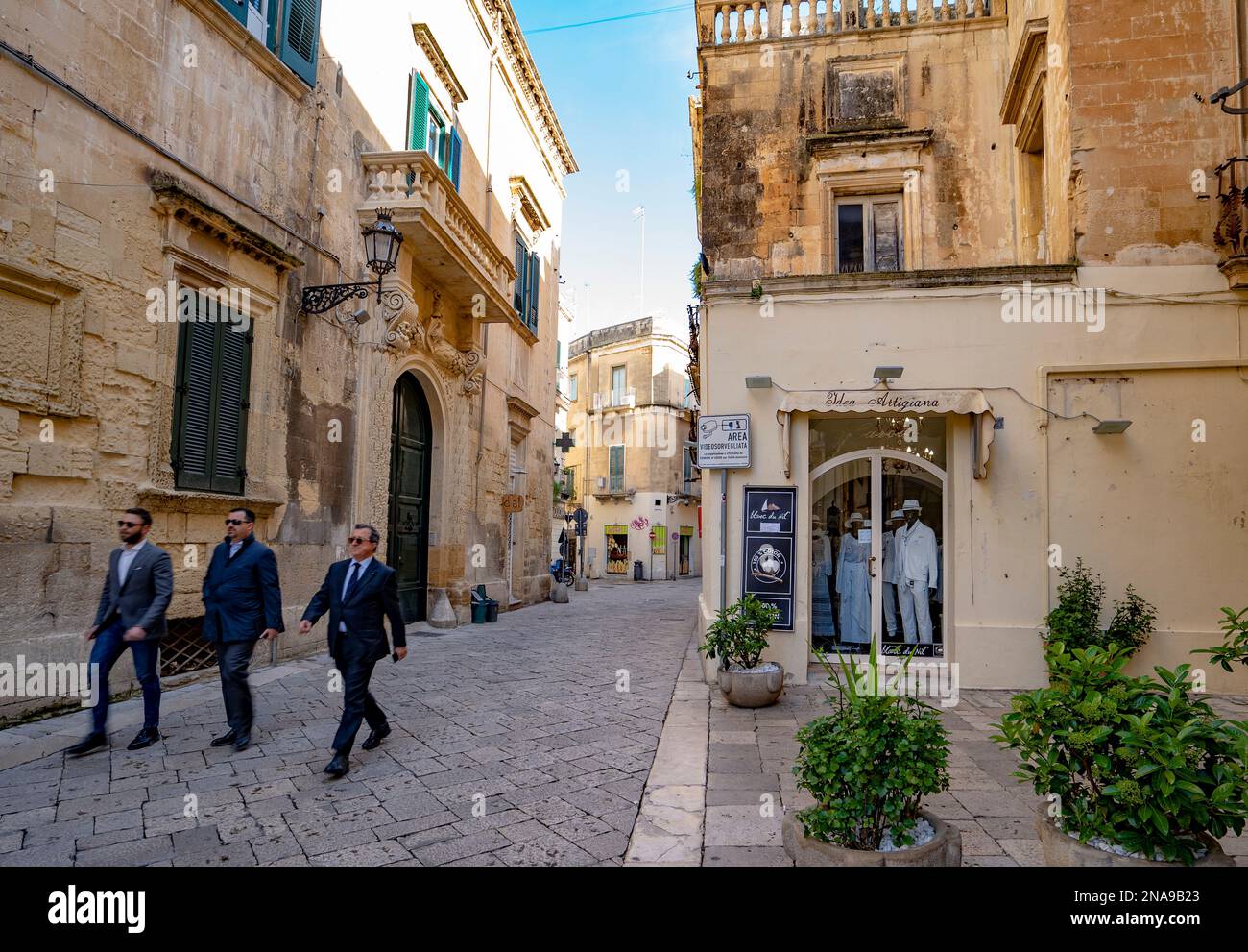 Tre uomini camminano nella piazza della città passando davanti ai negozi del centro storico di Lecce, Italia; Lecce, Puglia, Italia Foto Stock