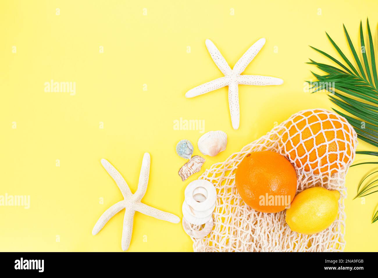 Stelle di mare, conchiglie con borsa a stringa con arance e limone con ramo di palma dal lato su sfondo giallo. Сoncept dell'ora legale, vacanza, tra Foto Stock