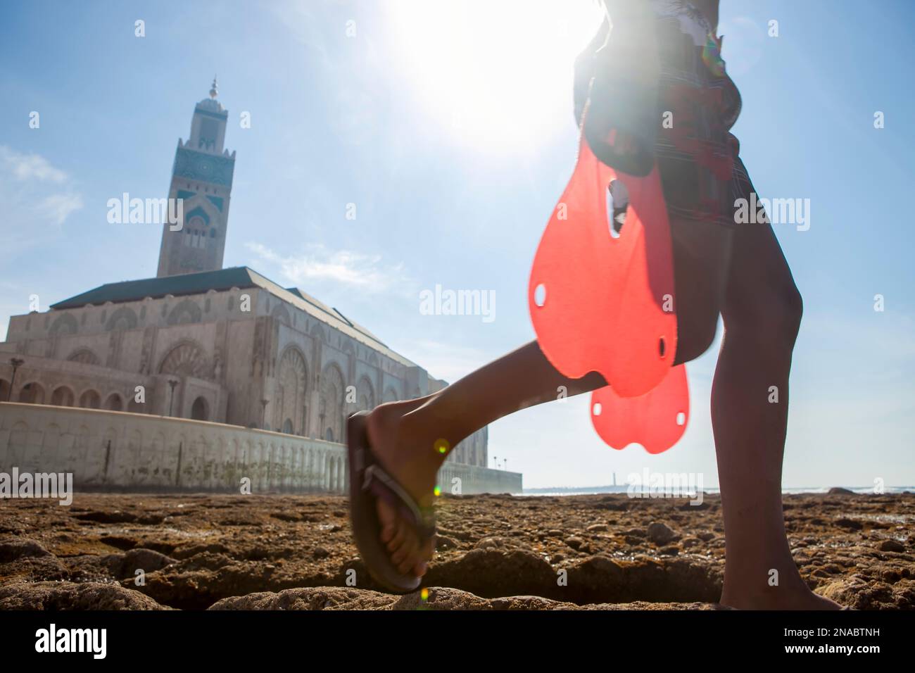 Di fronte alla moschea Hassan II di Casablanca, un giovane ragazzo porta le pinne per nuotare e fare immersioni in Marocco; Casablanca, Marocco Foto Stock