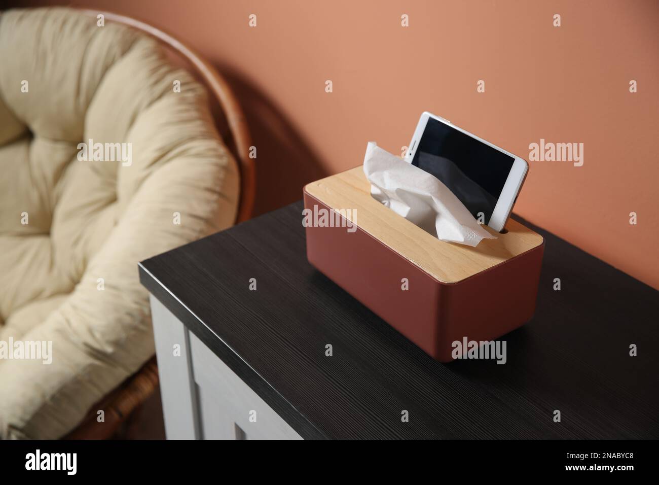 Scatola con fazzolettini di carta e smartphone su armadietto di legno in camera Foto Stock