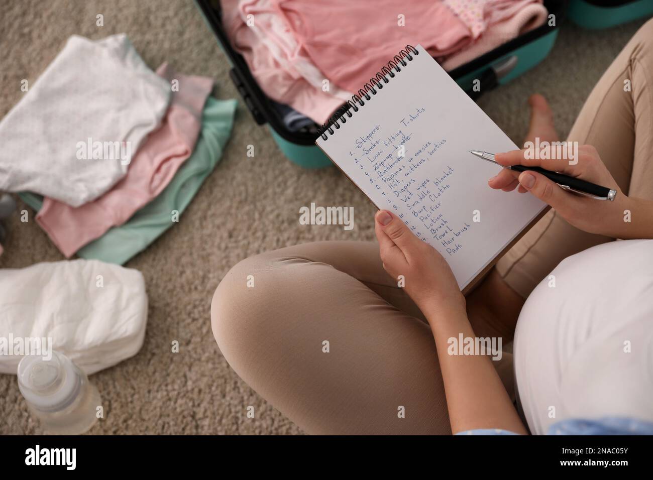 Donna incinta scrivere la lista di imballaggio per l'ospedale di maternità a casa, vista sopra Foto Stock