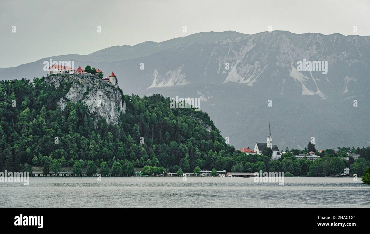 Lago di Bled con un castello di Bled in cima alla roccia e la chiesa Zupnijska cerkev svetega Martina - Chiesa di San Martina, Bled, cielo sfondo grigio Foto Stock