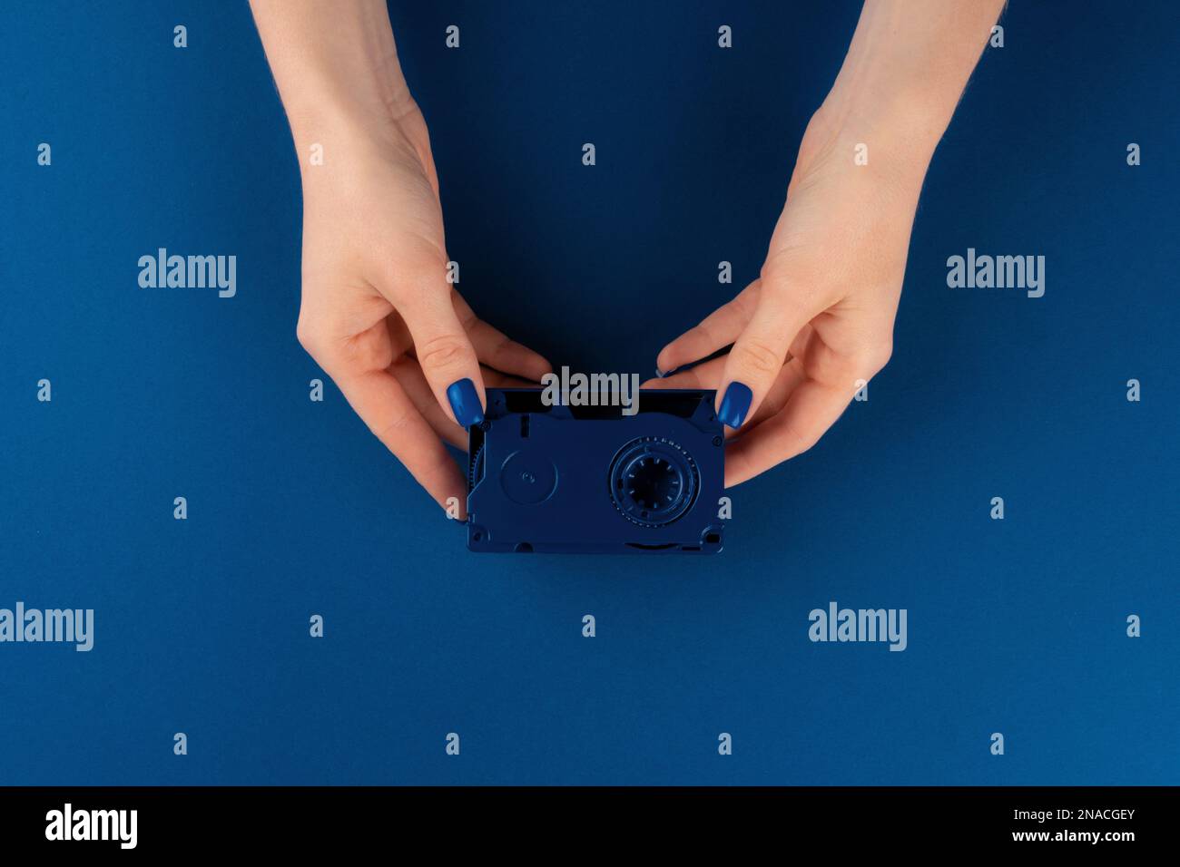 Mini videocassetta in mani femminili su sfondo blu classico Foto Stock