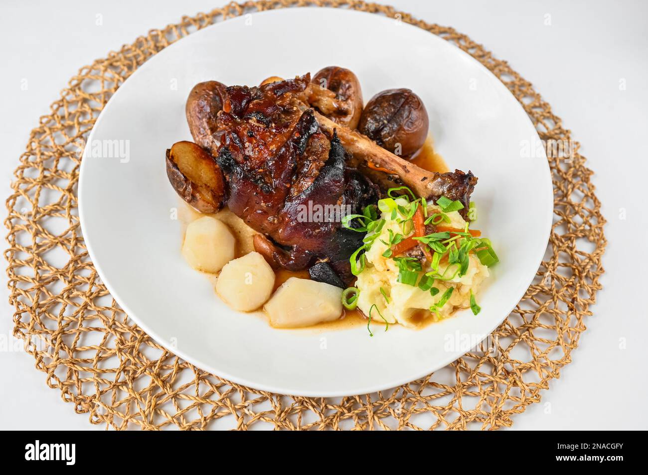 Ginocchio di maiale al forno con purè di patate e topinambur sul piatto, tampone di bambù su sfondo bianco. Foto Stock