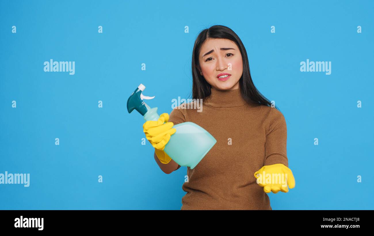 Rovesciare il detergente per la casa indossando guanti di gomma gialla mentre si mostra spray detergente chimico davanti alla fotocamera, spiegando l'efficienza del prodotto. Il housekepper professionale ha lavorato duro per effettuare una sede pulita Foto Stock