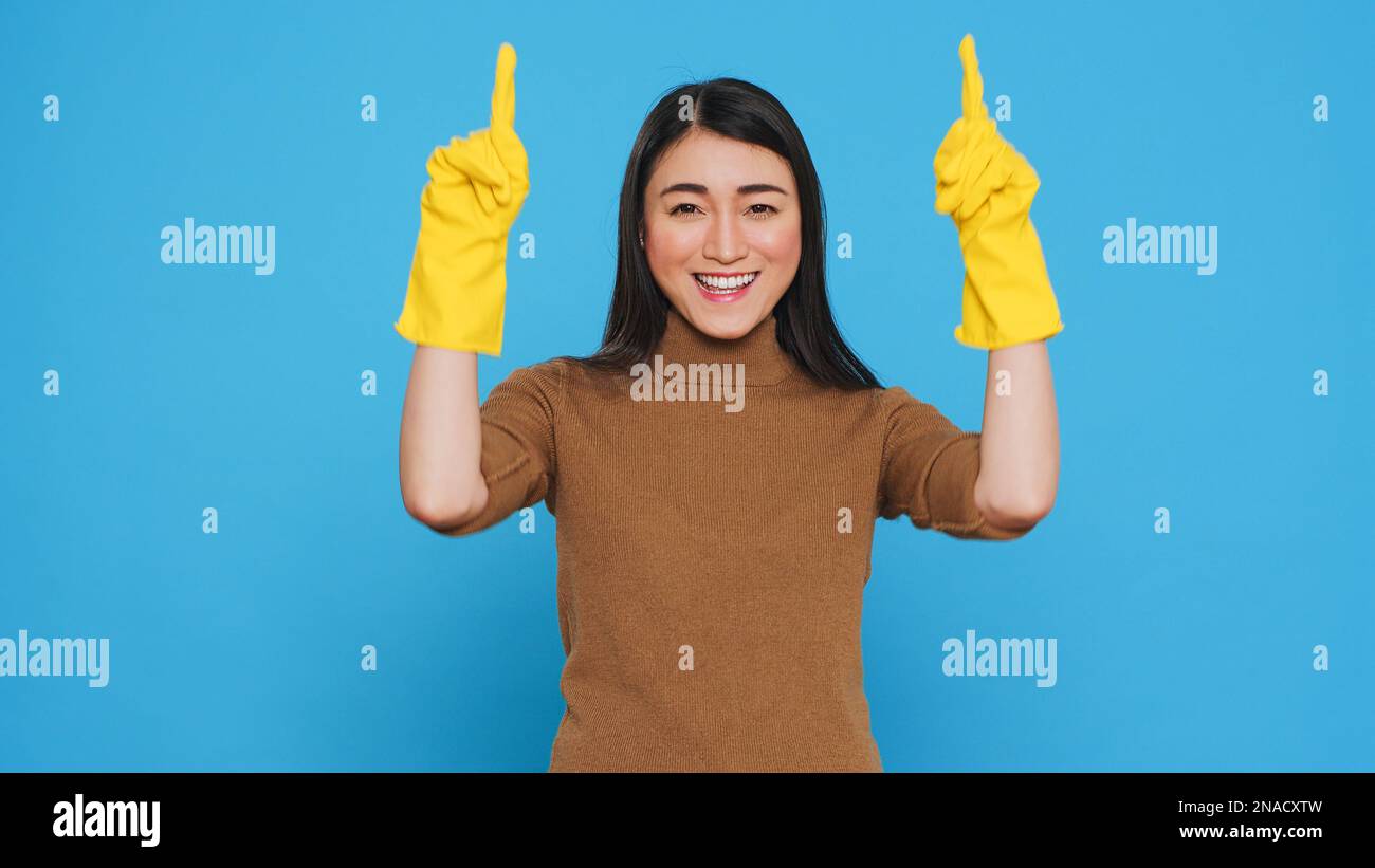 Housekepper professionale che punta e mostra la pubblicità di pulizia o testo isolato, in piedi su sfondo blu in studio. Casalinga ha lavorato duro per effettuare una casa pulita, usando i prodotti di igiene Foto Stock