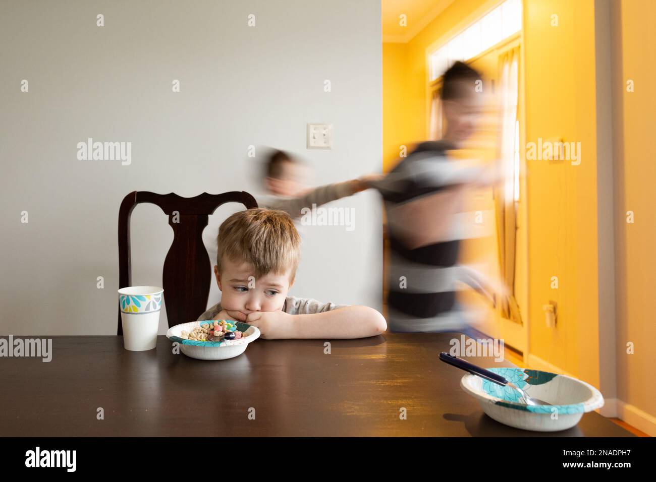 Sad Boy si siede fissando il tavolo mentre i Fratelli girano dietro di lui Foto Stock