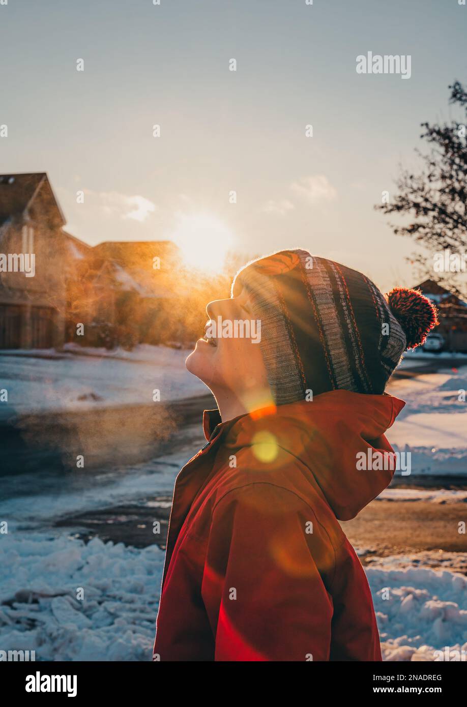 Ragazzo in cappello e cappotto d'inverno che esalano aria gelida nella giornata invernale di sole. Foto Stock