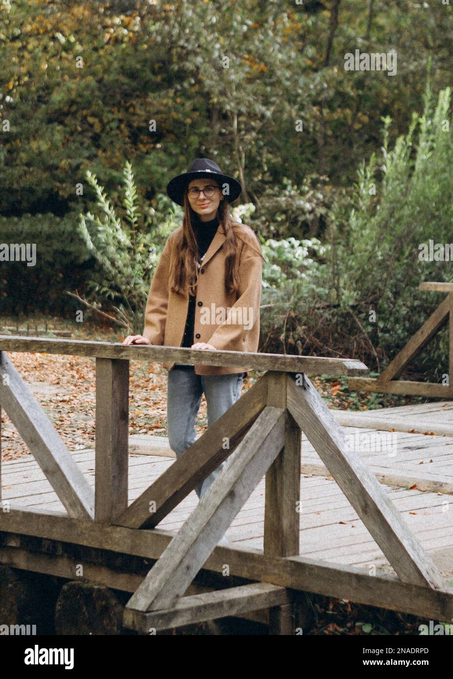 giovane donna in giacca marrone e cappello nero nella foresta Foto Stock