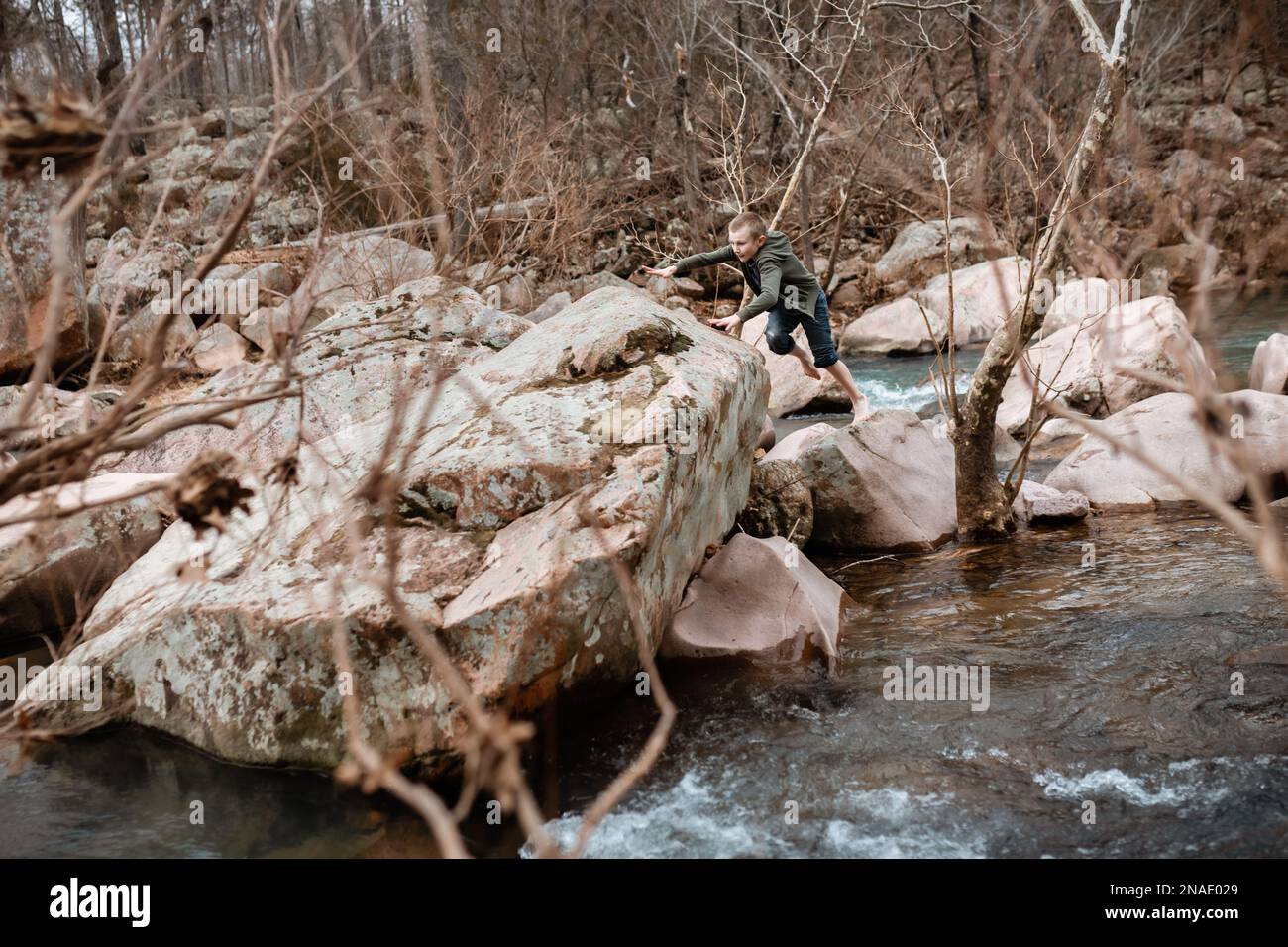 Giovane ragazzo che salta sopra le rocce sul fiume Foto Stock