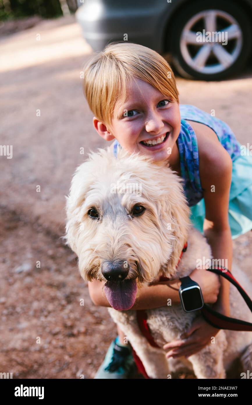 Il bambino abbraccia felicemente il suo cane bianco dorato del doodle in estate Foto Stock