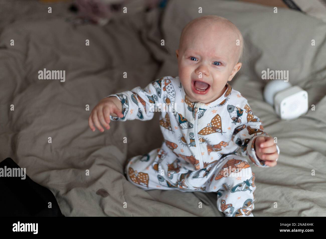 Bambino piangente seduto sul letto con lenzuola grigie Foto Stock