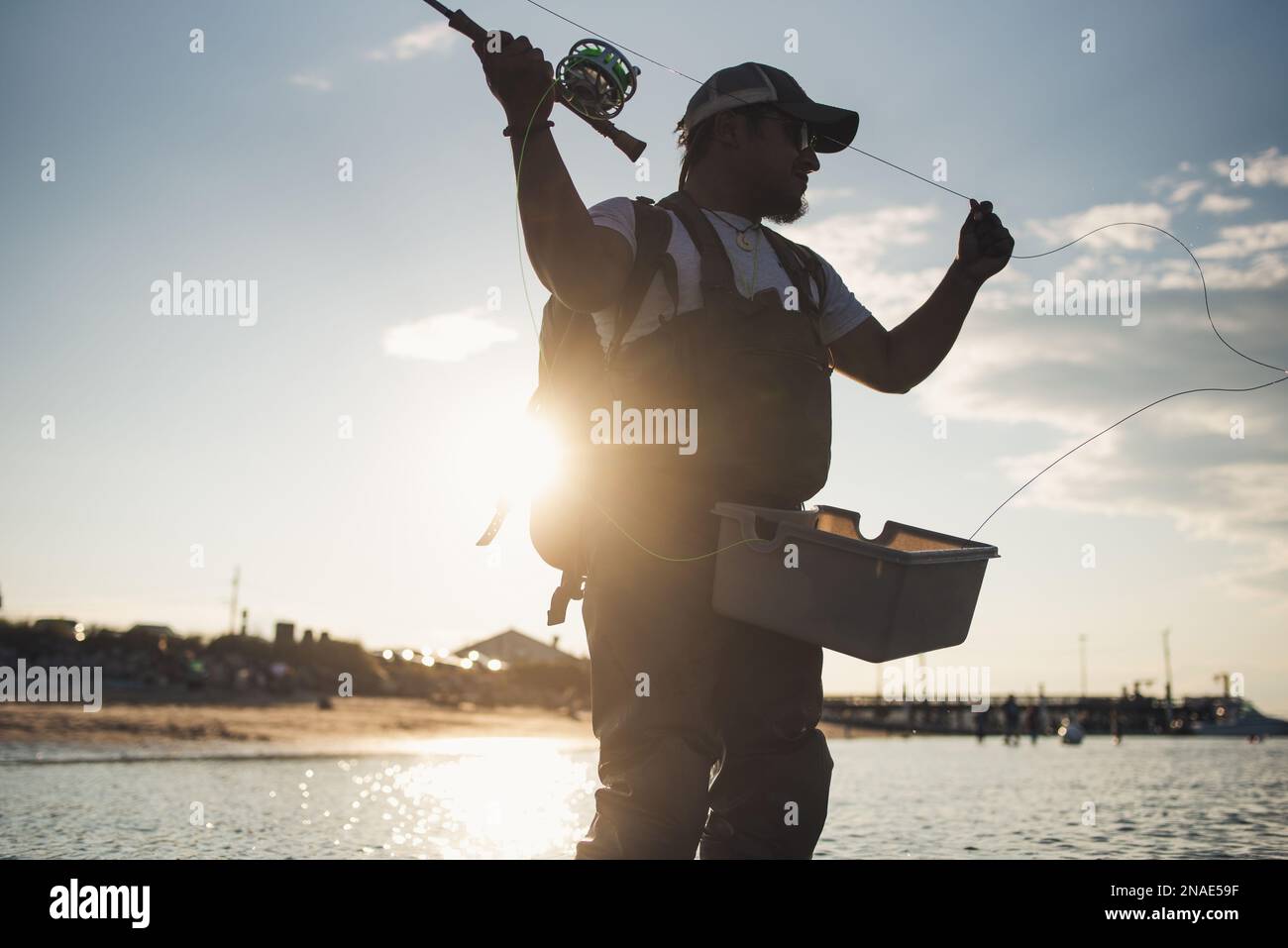 Uomo ispanico pesca a mosca in oceano al largo della spiaggia nel pomeriggio Foto Stock
