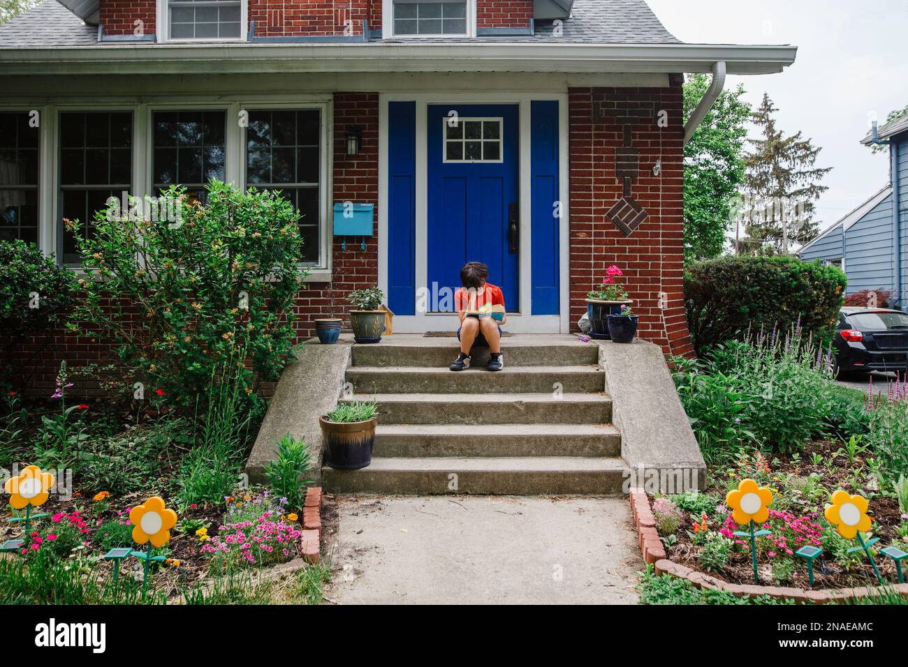 Un bambino irriconoscibile si siede sul punto di partenza di casa che legge un libro Foto Stock