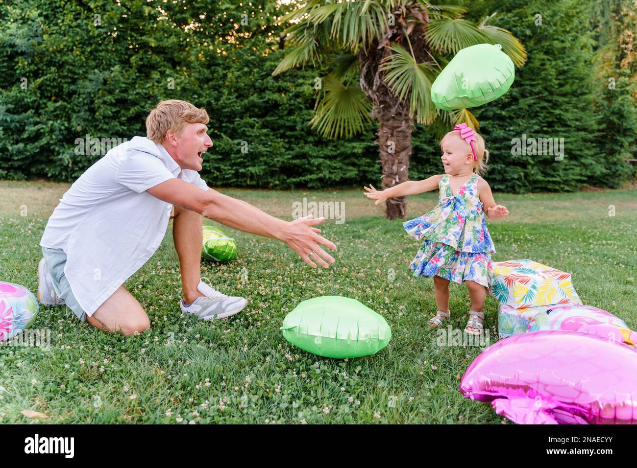 Bambino di due anni che gioca con papà in un pallone sull'erba Foto Stock